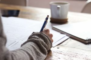 Woman in sweater writing on paper with pen