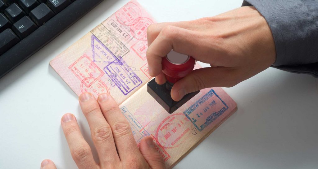 Person stamping passport book whose pages are covered in colorful stamps of other countries